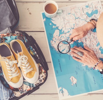 person looking down at a map with coffee a suitcase and yellow shows in the suitcase